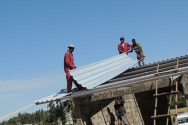 Traja etiópski robotníci pokrývajú strechu vlnitým plechom
