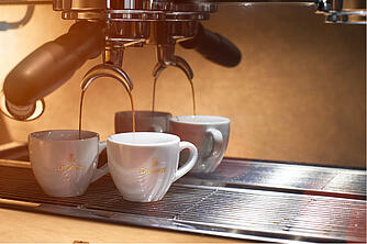 Iš aparato su sietelio laikikliu pagaminta espresso kava bėga į du baltus espresso puodelius