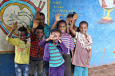 Besijuokiantys Etiopijos vaikai stovi prieš spalvingą sieną ir mojuoja